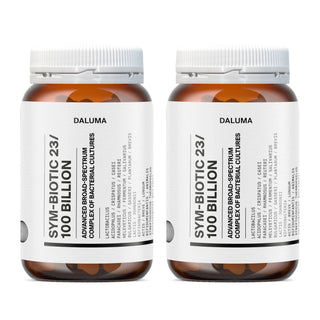 Zwei braune DALUMA SYM-BIOTIC 23/100 BILLION DARMBAKTERIEN DOUBLE Flaschen mit weißen Etiketten heben Informationen über Lactobacillus Bakterienkulturen und lebende Bakterienkulturen in schwarzer Schrift hervor. Die Flaschen werden nebeneinander gestellt.