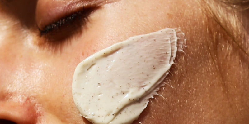 Eine Nahaufnahme des Gesichts einer Person mit geschlossenen Augen und einer dicken Schicht Creme mit sichtbaren Flecken auf der Wange.