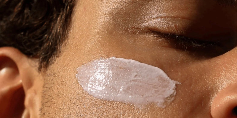 Eine Nahaufnahme des Gesichts einer Person mit geschlossenen Augen, auf deren Wange eine dicke Schicht weißer Creme oder Lotion aufgetragen ist.