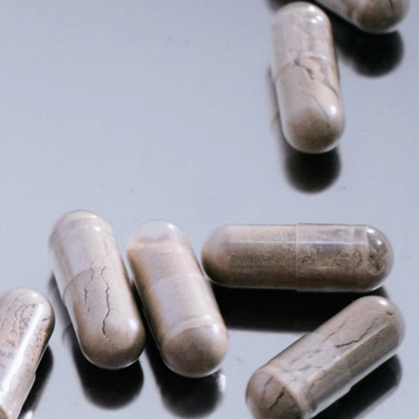 Mehrere braune, marmorierte Kapseln sind auf einer spiegelnden Oberfläche verstreut. Die Kapseln erscheinen glänzend und sind in verschiedenen Ausrichtungen dargestellt.