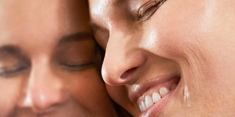 Nahaufnahme von zwei lächelnden Menschen, deren Gesichter sich berühren. Beide wirken glücklich und entspannt, mit glatter Haut und geschlossenen Augen, die ein Gefühl von Wärme und Nähe vermitteln.