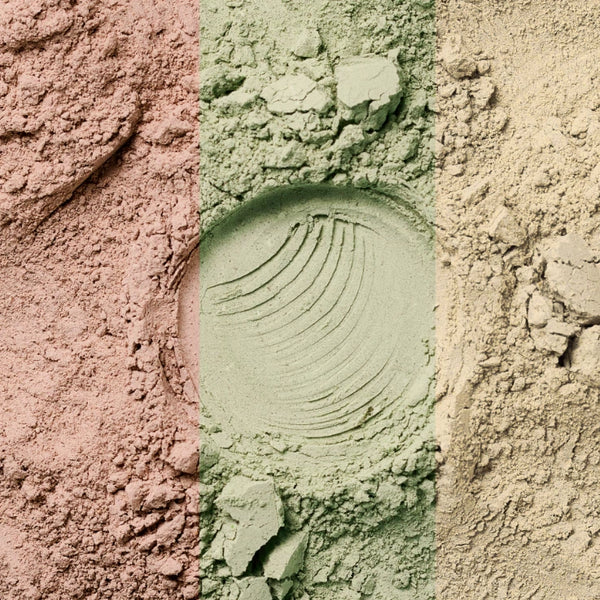 Drei vertikale Abschnitte mit verschiedenfarbigen Pulvern - rosa, grün (mit einem kreisförmigen Abdruck in der Mitte) und beige - sind nebeneinander angeordnet, mit sichtbarer Textur und kleinen Klumpen.