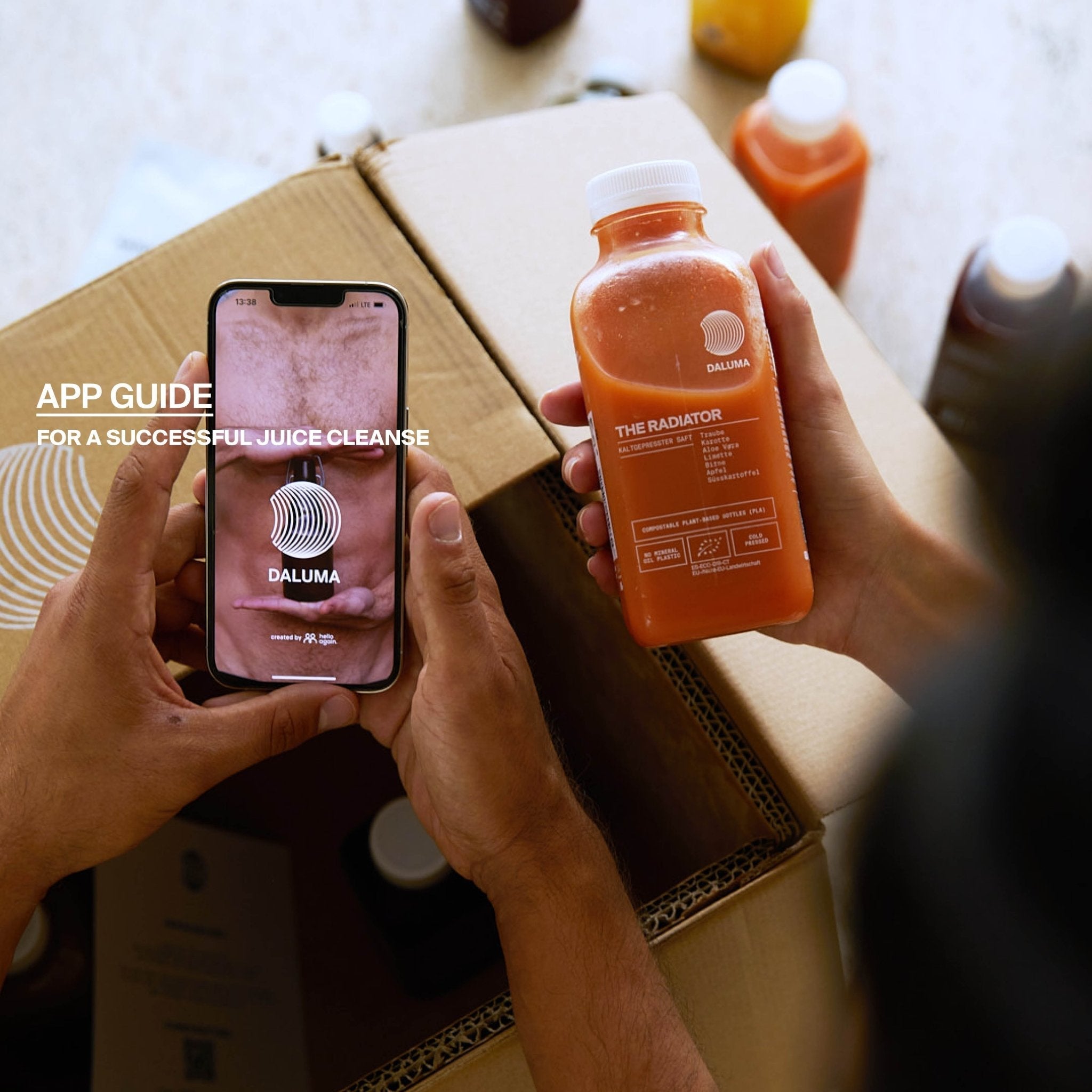 Eine Person hält ein Smartphone mit dem BETTER ENERGY SAFTKUR 3 TAGE Ratgeber von DALUMA und eine Orangensaftflasche, umgeben von bio-kaltgepressten Säften und Kisten mit unpasteurisiertem Kombucha im Hintergrund.