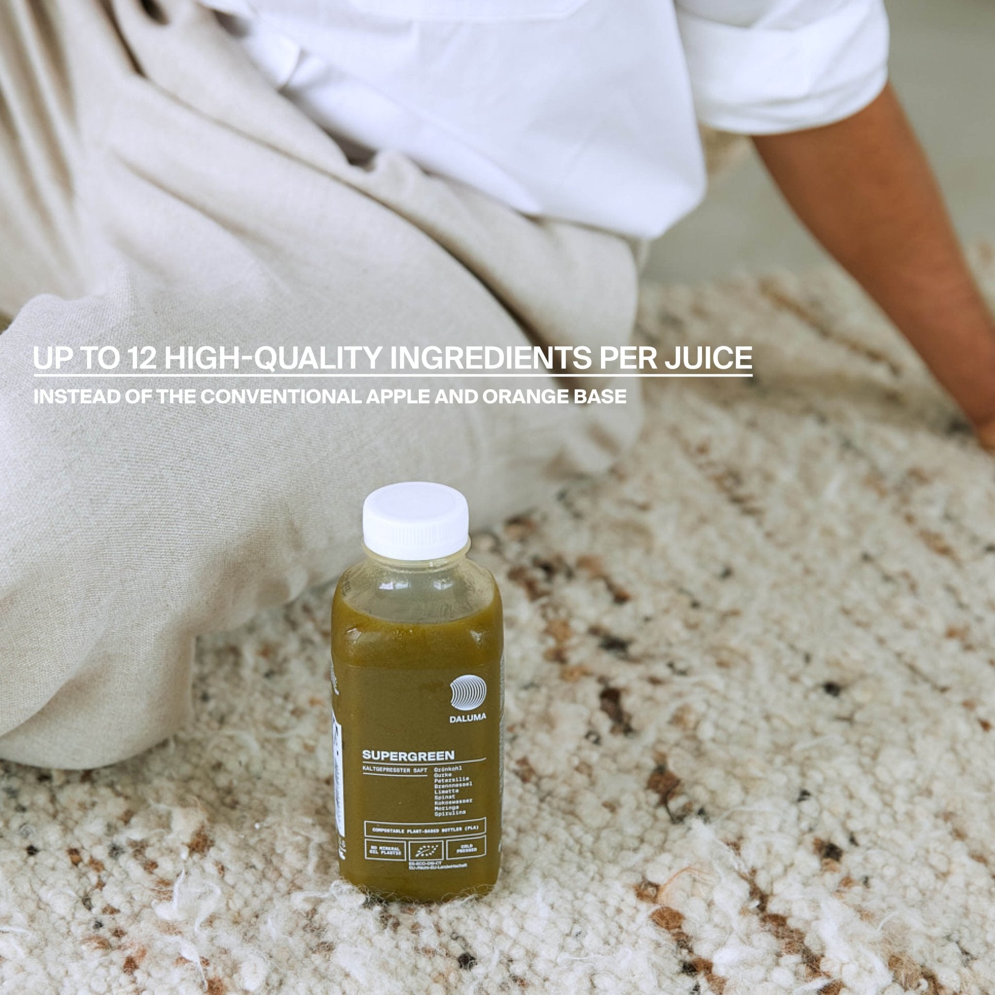 Eine Flasche DALUMA BETTER ENERGY SAFTKUR 5 TAGE steht auf einem beigen Teppich neben einer Person in hellen Hosen. Text: Bis zu 12 hochwertige Zutaten pro Saft - bio-kaltgepresste Säfte, nicht nur Apfel und Orange.