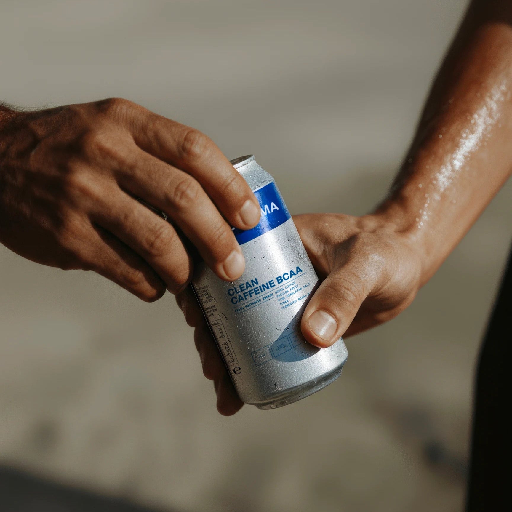 Zwei Hände tauschen eine silberne DALUMA ENERGY & BALANCE DUO Dose mit blauen Akzenten aus, beide leicht verschwitzt - und fangen den erfrischenden Schub an natürlicher Energie nach intensiver Aktivität ein.