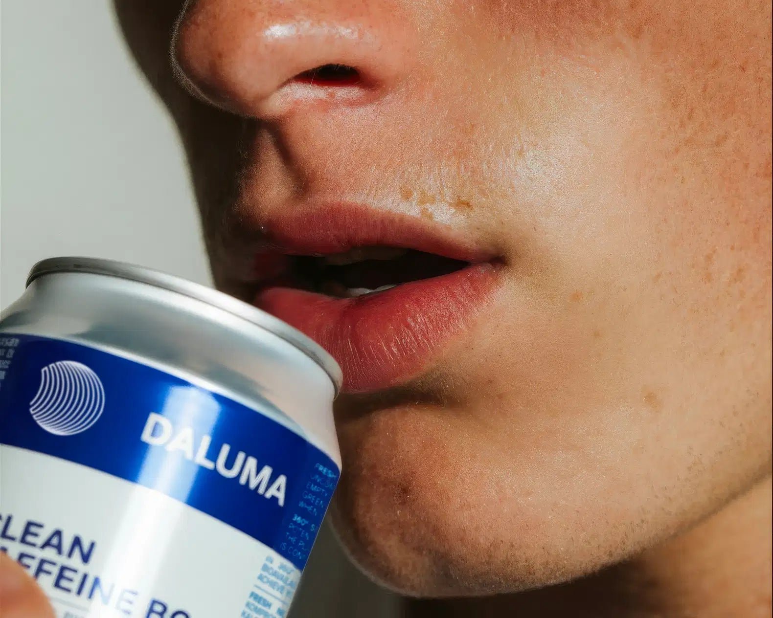 Eine Nahaufnahme zeigt eine Person, die eine geöffnete Dose DALUMA ENERGY & BALANCE DUO an ihre Lippen hält. Auf dem blau-weißen Etikett steht 