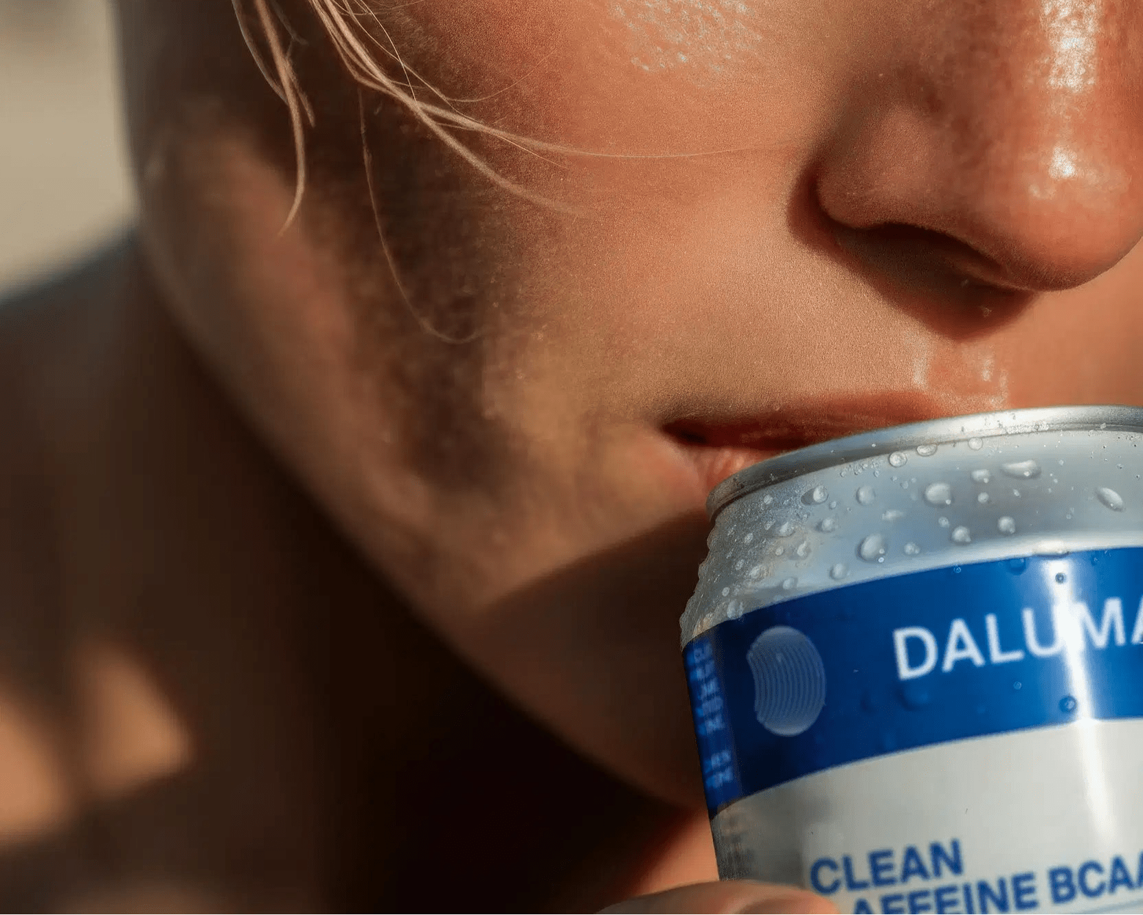 Nahaufnahme einer Person, die eine DALUMA ENERGY & BALANCE DUO Dose an die Lippen hält, wobei das Sonnenlicht Schatten auf die Haut wirft und die natürliche Energie in jedem Schluck sichtbar wird.
