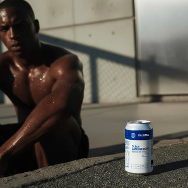 Ein Mann in Trainingskleidung sitzt im Freien und hat eine Dose DALUMA CLEAN BCAA ENERGY DRINK 6 PACK - ein natürliches Energiegetränk mit veganen BCAAs - vor sich auf den Betonboden gestellt.