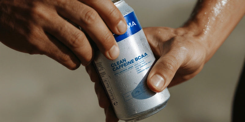 Eine Person mit feuchten Händen hält eine silberne Dose mit der Aufschrift Clean Caffeine BCAA mit blauen Akzenten und Nährwertangaben und bereitet sich darauf vor, sie zu öffnen.