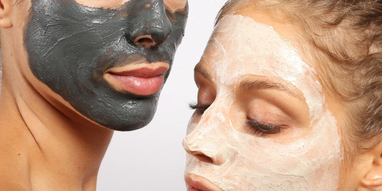 Zwei Personen mit Gesichtsmasken: eine mit einer dunklen Holzkohlemaske und die andere mit einer hellen Tonmaske. Beide haben die Augen geschlossen und zeigen glatte Haut und einen entspannten Gesichtsausdruck vor einem neutralen Hintergrund.