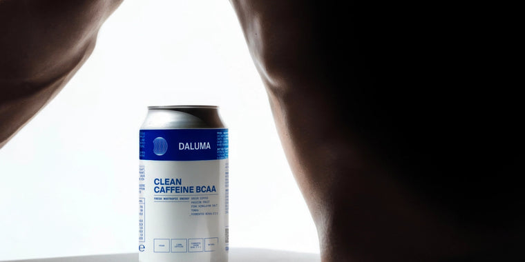 Eine Dose mit der Aufschrift DALUMA Clean Caffeine BCAA ist zwischen zwei muskulösen, nackten Armen oder Beinen positioniert, wobei ein strahlend weißer Hintergrund das Produkt hervorhebt.