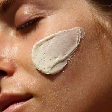 Eine Nahaufnahme des Gesichts einer Person mit geschlossenen Augen, auf deren Wange die CLEANSE AND HYDRATE MASK DUO 3 PACK von DALUMA als dicke, cremige Schicht für tief durchfeuchtete Haut aufgetragen ist.