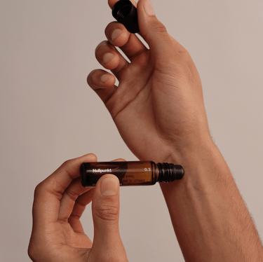 Eine Person hält einen Braunglas-Rollerball-Flakon aus der NULLPUNKT COMPLETE COLLECTION von Nullpunkt in der Hand und nimmt die schwarze Kappe vor einem minimalistischen, neutralen Hintergrund ab.