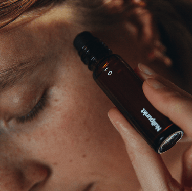 Eine Person hält eine kleine dunkle Glastropfflasche mit der Aufschrift NULLPUNKT GRADE 0.1 RELIEVE von Nullpunkt in der Nähe ihres Gesichts, die Augen geschlossen und gelassen, was auf eine beruhigende Hautpflege oder Aromatherapie hindeutet.