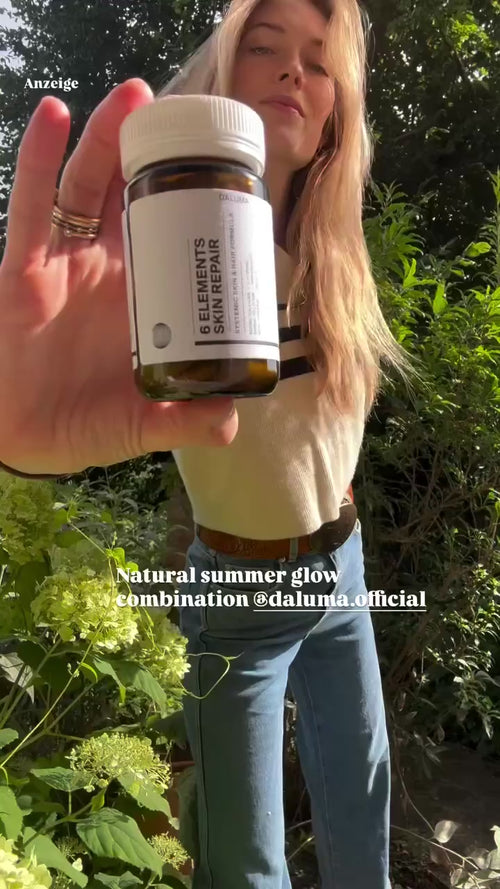 Eine Frau steht im Freien in einem Garten und hält eine braune Flasche mit der Aufschrift 6 Elements Skin Repair in die Kamera. Der Text auf dem Bild lautet: "Natural summer glow combination @daluma.official.