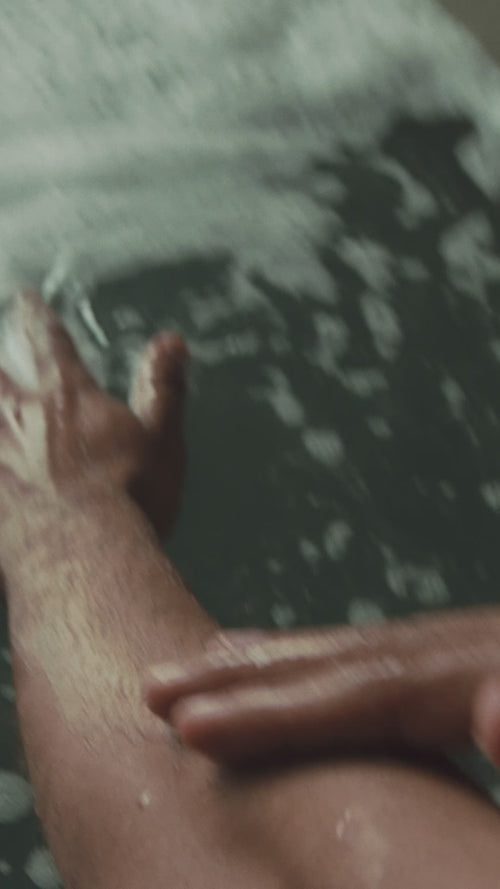 Eine Nahaufnahme zeigt eine Person, die das HAIR CARE DUO von Daluma über einer mit Wasser und Blasen gefüllten Badewanne auf ihr Bein aufträgt.