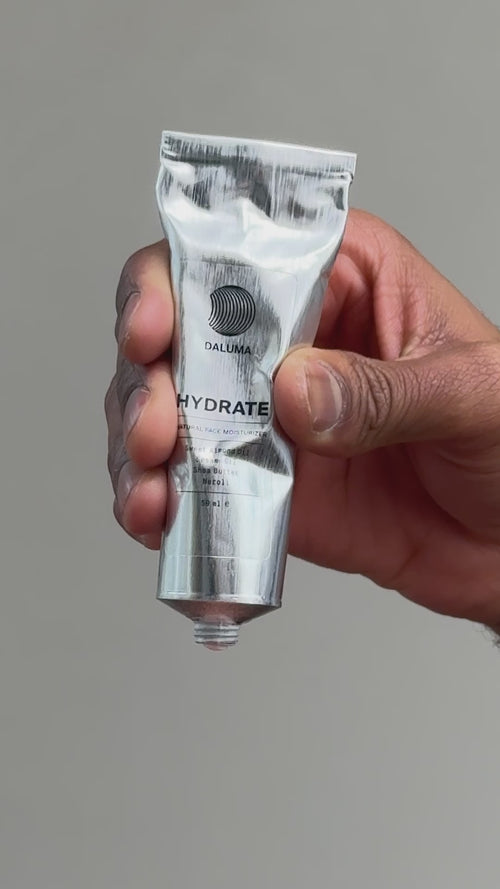 Eine Hand hält eine Metalltube mit der Aufschrift DALUMA HYDRATE vor einem schlichten grauen Hintergrund. Die Kappe ist abgenommen, so dass die Öffnung der Tube zu sehen ist.