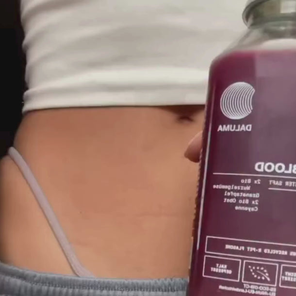 Nahaufnahme des Unterleibs einer Person in einem hellvioletten Hosenbund, die eine mit violetter Flüssigkeit gefüllte Flasche Daluma BETTER SHAPE SAFTKUR 3 TAGE Saft hält.