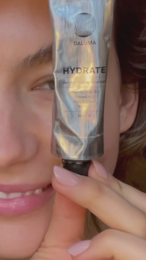 Eine Person hält ein Metallröhrchen mit der Aufschrift DALUMA HYDRATE nahe an ihr Gesicht, wobei im Hintergrund ein Teil ihres Gesichts und ein sanftes Lächeln zu sehen sind.