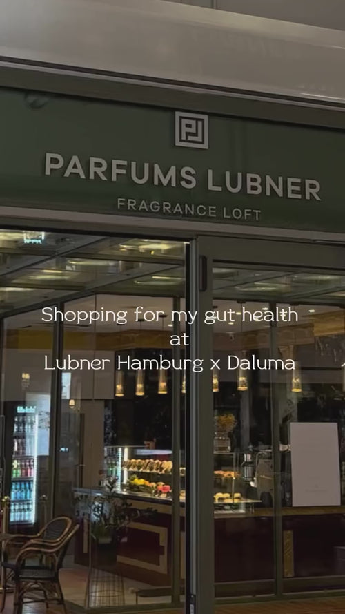 Schaufenster von Parfums Lubner mit Glastüren und Licht im Inneren. Weißer Text überlagert: "Einkaufen für meine Darmgesundheit - bei Lubner Hamburg x Daluma." Ein Display mit Produkten ist durch das Fenster sichtbar.