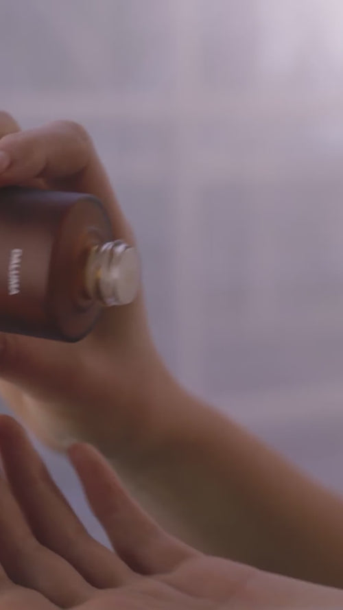 Eine Person gießt Dalumas GREEN COFFEE CLEANSER ENZYMPEELING aus einer braunen Flasche in ihre Handfläche, mit einem leicht verschwommenen Hintergrund.